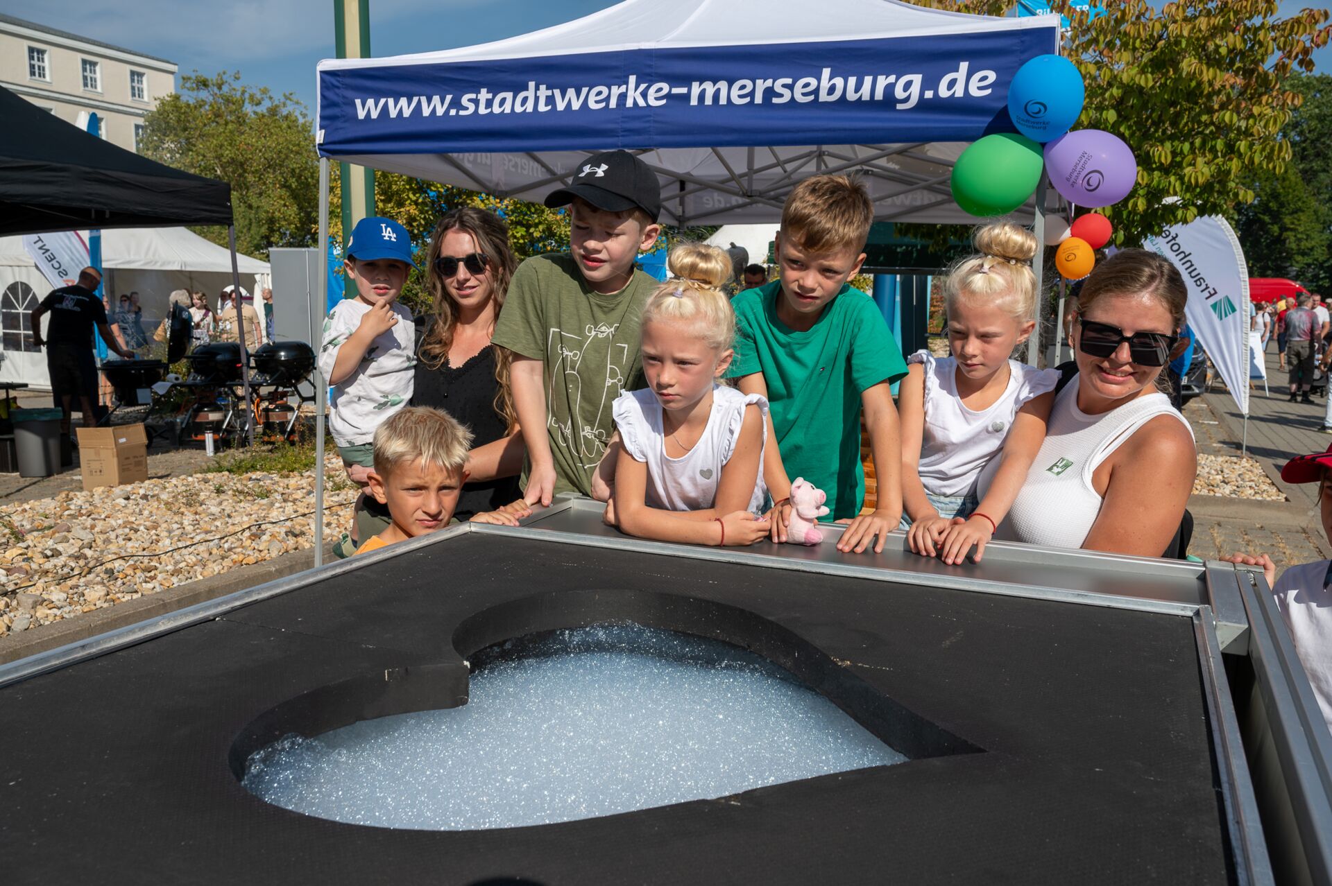 Auf diesem Bild sehen Sie eine Gruppe von Kindern, mit 2 Erwachsenen, welche sich eine Attraktion beim Tag der offenen Tür anschauen.