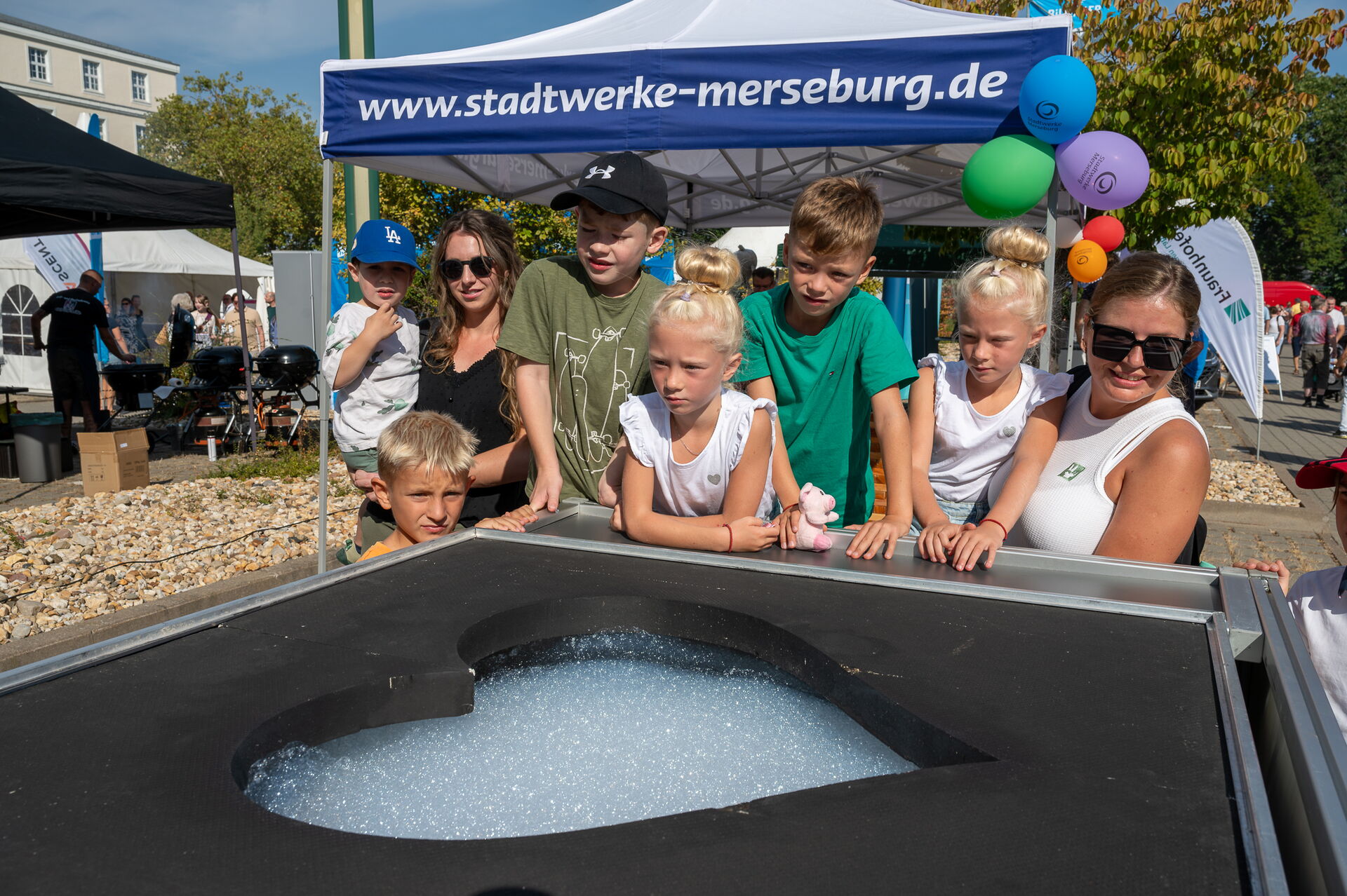 Auf diesem Bild sehen Sie eine Gruppe von Kindern, mit 2 Erwachsenen, welche sich eine Attraktion beim Tag der offenen Tür anschauen.
