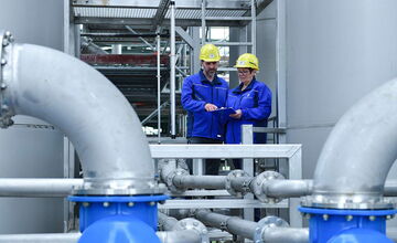 Auf diesem Bild sehen Sie zwei Personen, welche die aktuellen Werte der Abwasseranlage prüfen.